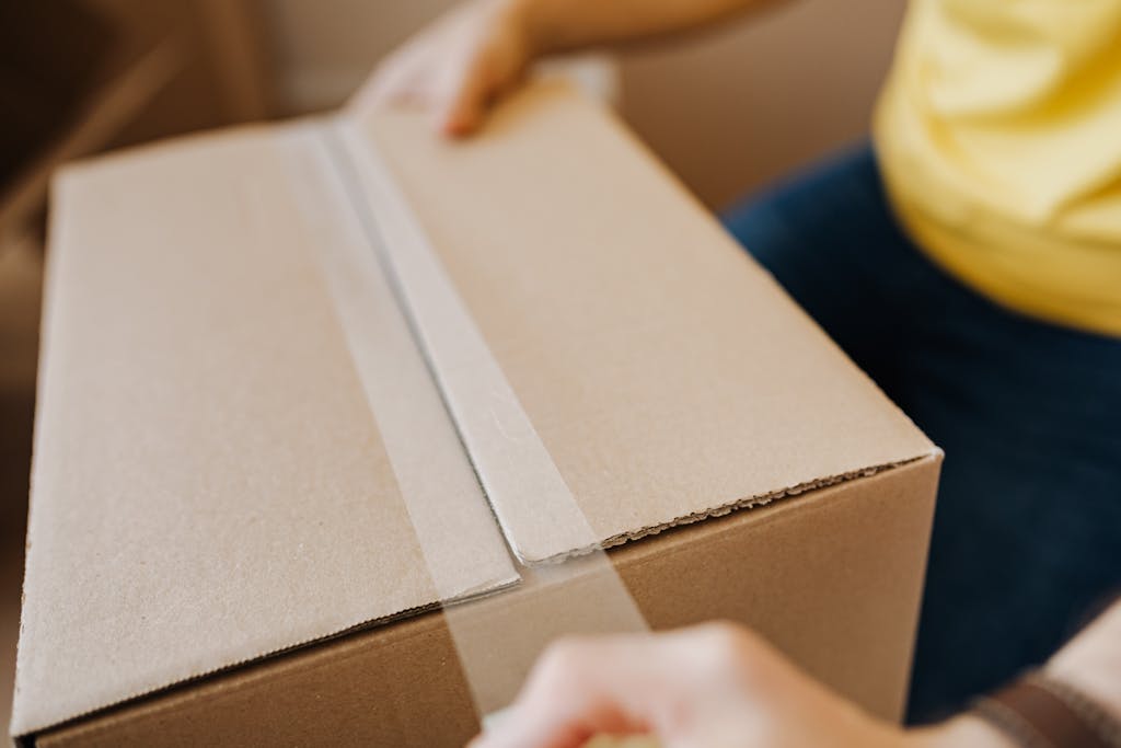 Close-up of a person sealing a cardboard box with tape, for a same day courier delivery.