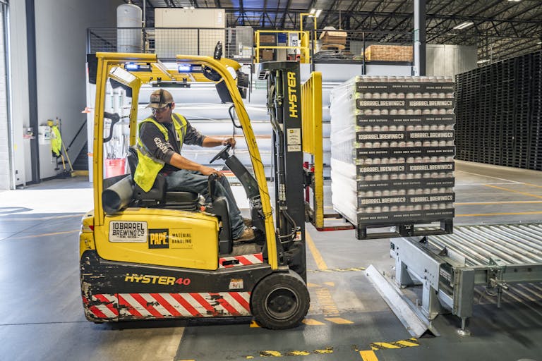 A warehouse worker maneuvers a forklift to transport crates with same day courier for manufacturing & engineering businesses.