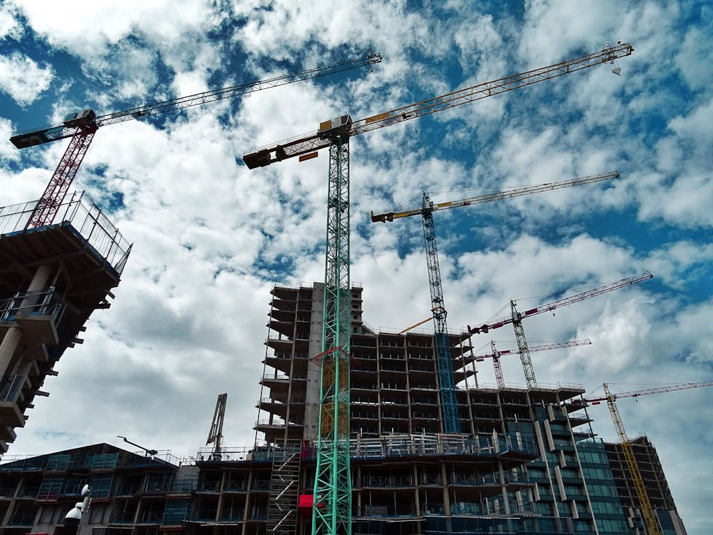 Urban construction site with numerous cranes framing rising skyscrapers against a blue sky. Same day courier delivery site.