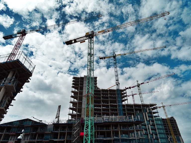 Urban construction site with numerous cranes framing rising skyscrapers against a blue sky. Same day courier delivery site.